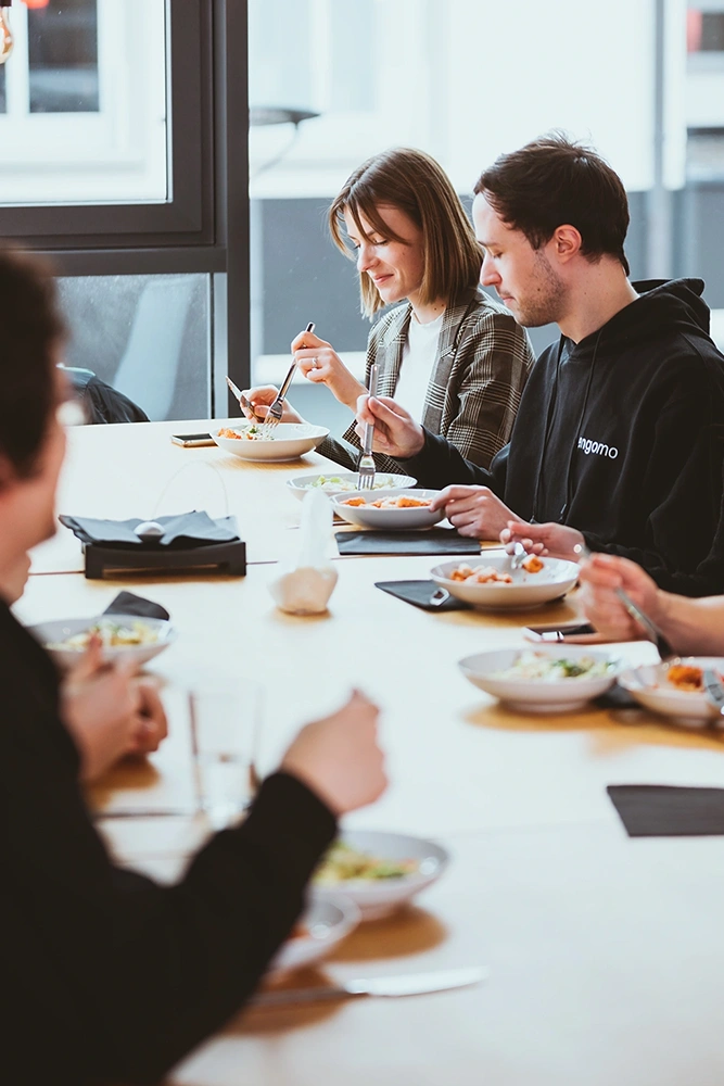 Several people sitting together at a table eating, in a bright and modern setting with large windows.