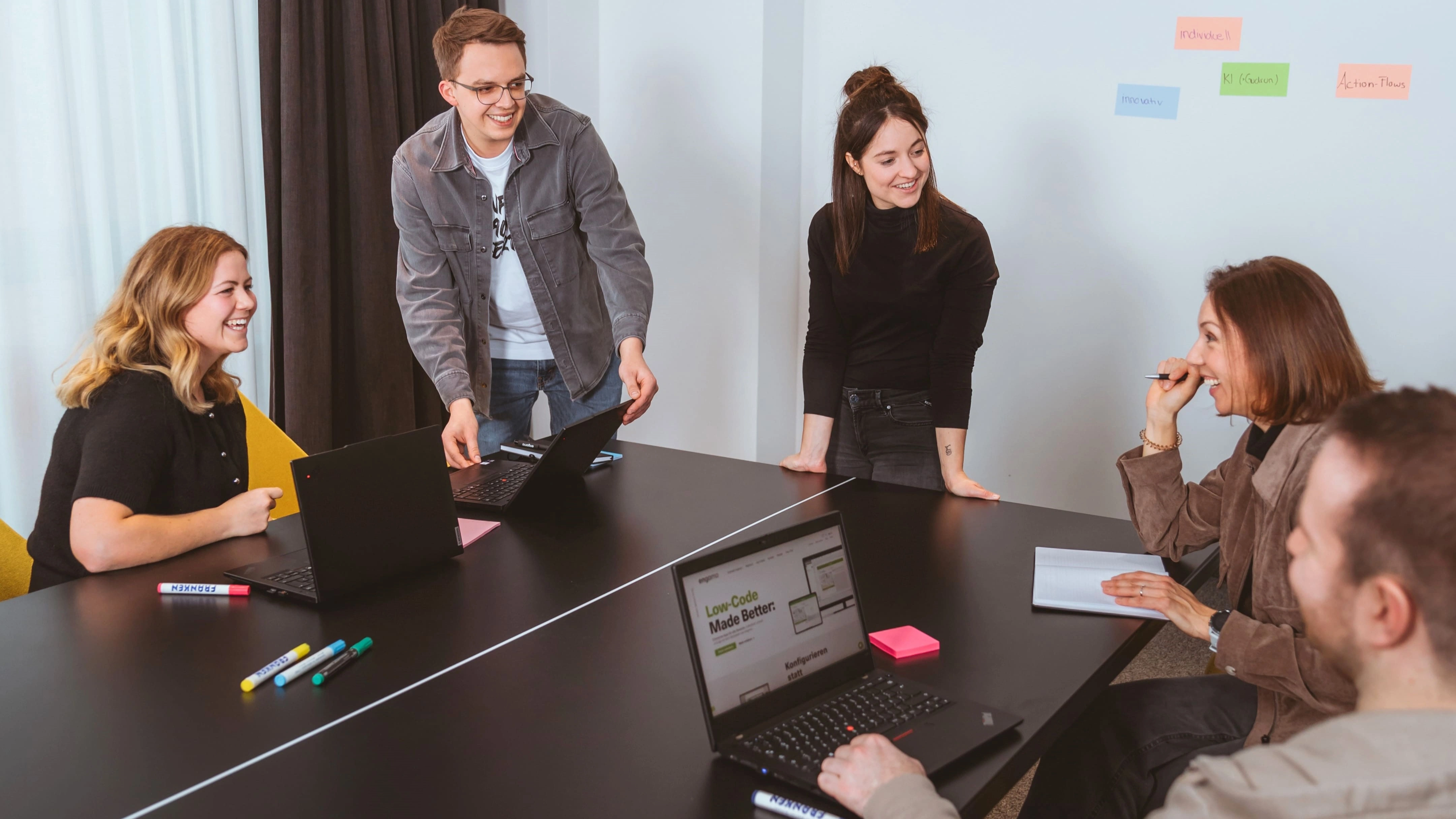 engomo-Team bei einem kreativen Meeting mit Laptops, Whiteboard und bunten Moderationskarten – symbolisiert Zusammenarbeit, Digitalisierung und Low-Code-Innovation.