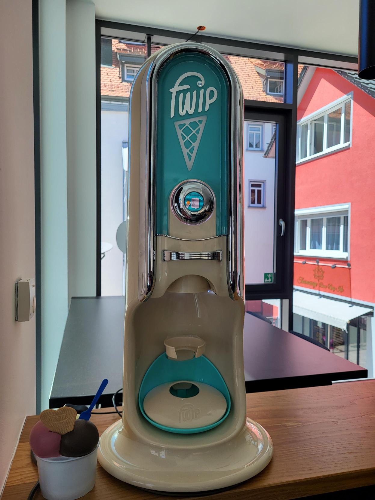 Eine große Gruppe von Mitarbeitenden trägt engomo-T-Shirts und sitzt und steht gemeinsam lachend für ein Gruppenfoto im modernen Büro.