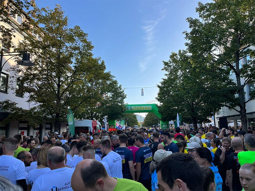 A large crowd of runners gathered at the start of a city race under a green archway