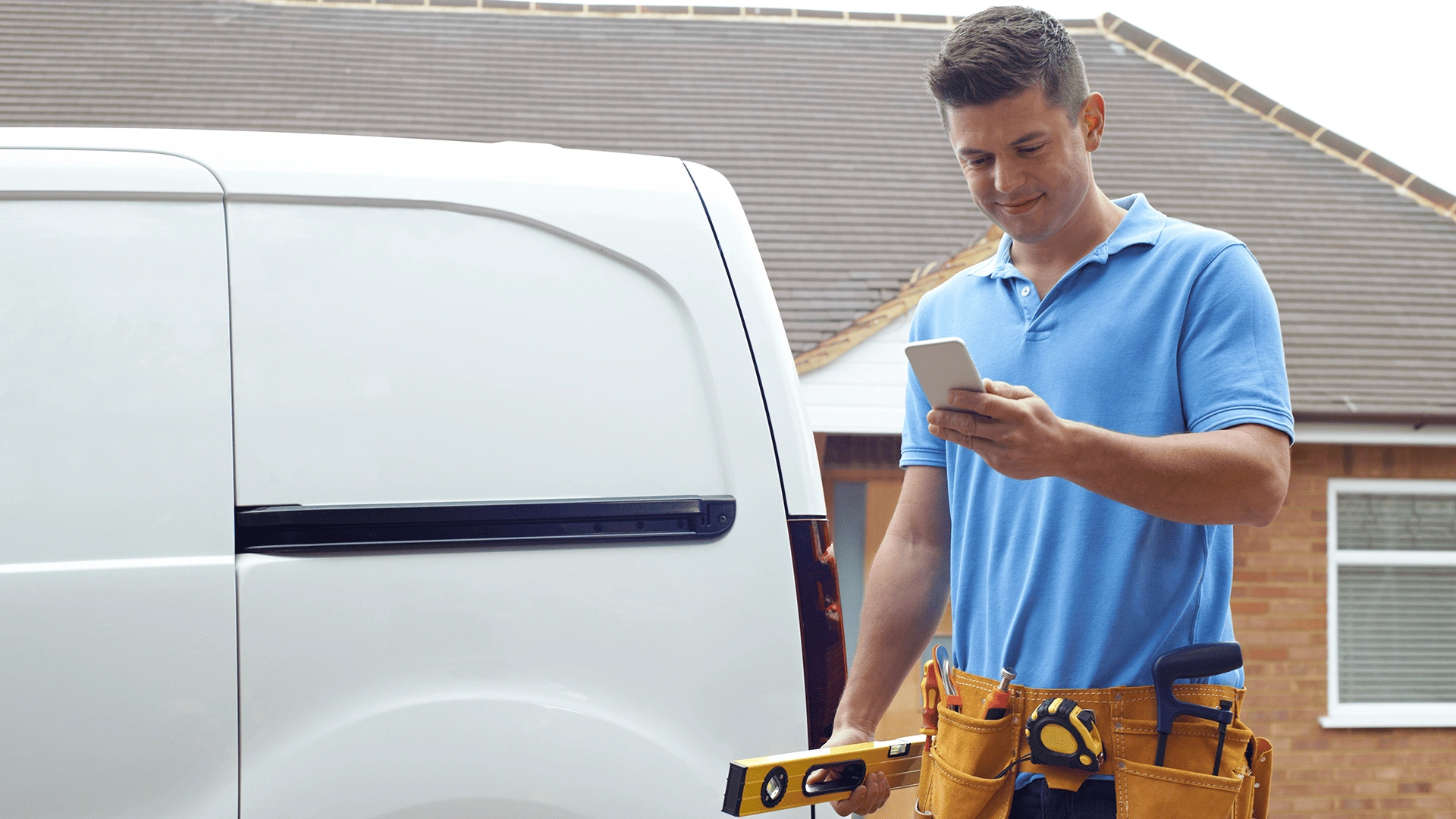 Service technician standing in front of a van using a smartphone – representing mobile field service operations with digital support.