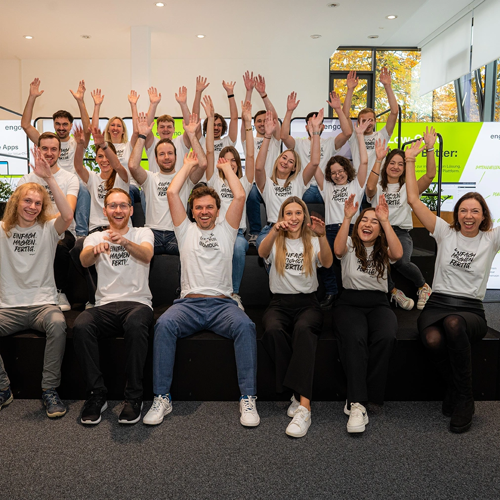 The image shows the engomo team sitting on a staircase, joyfully raising their hands in the air
