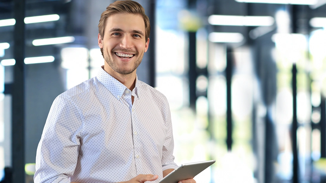 Sales representative in a business environment holding a tablet and smiling at the camera – representing mobile CRM and digital sales processes.