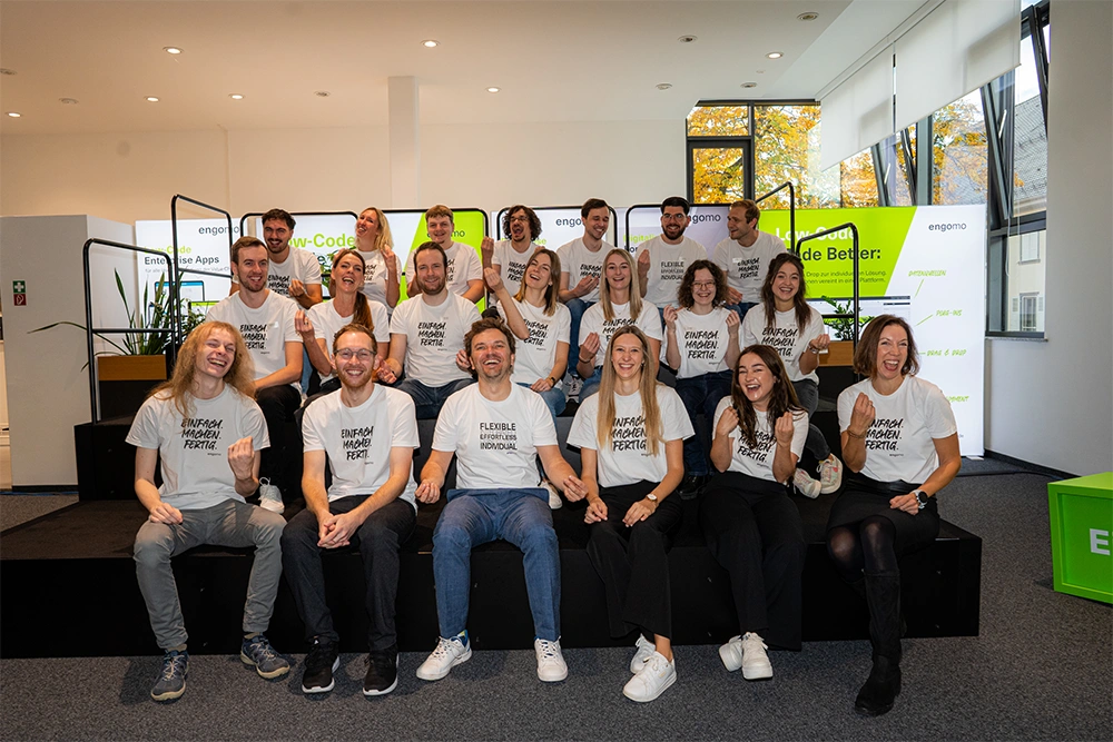 Das Bild zeigt das engomo-Team auf einer Treppe sitzend und freudig in die Kamera lachend