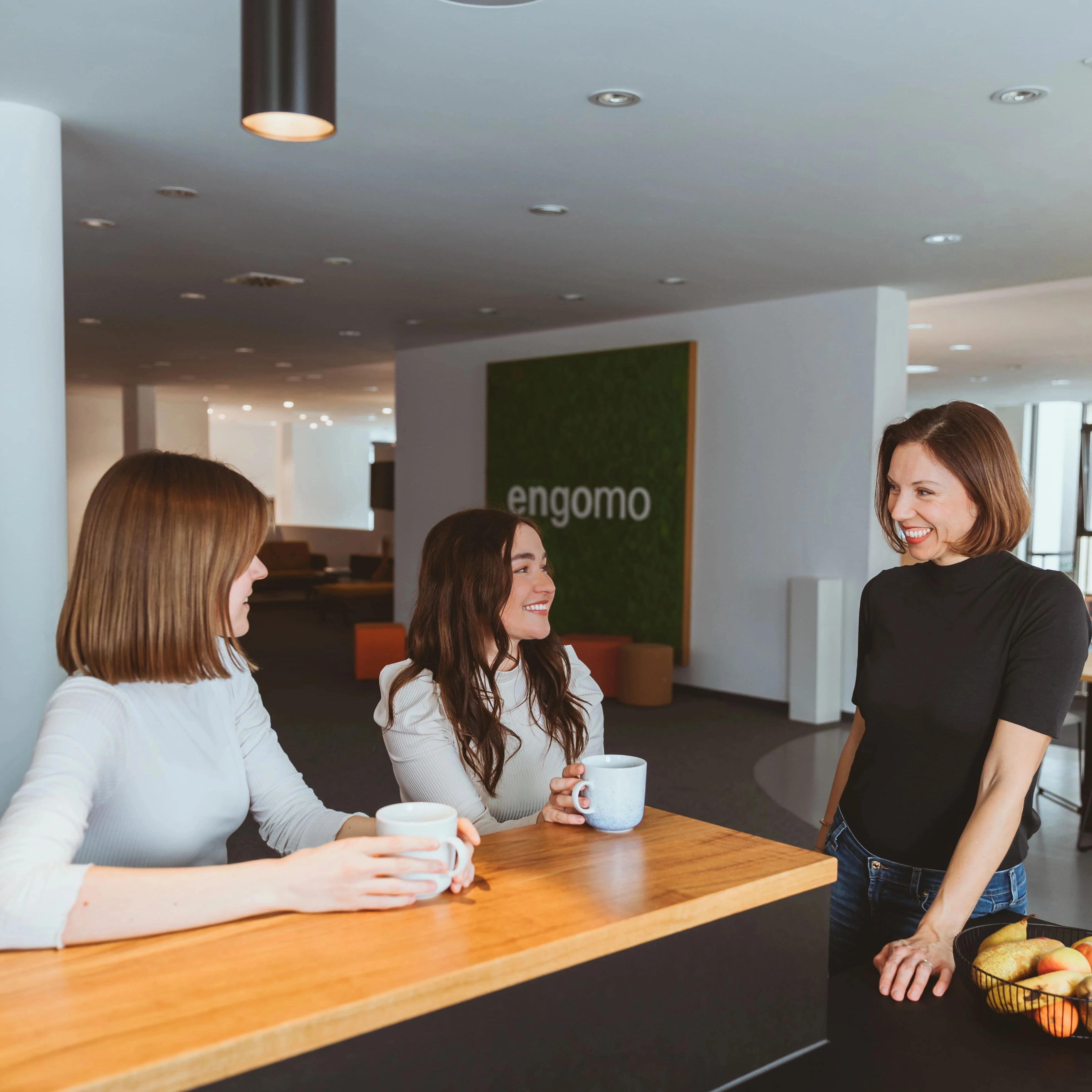 Drei Mitarbeiterinnen stehen zusammen an einer Küchenzeile und unterhalten sich bei Kaffee.