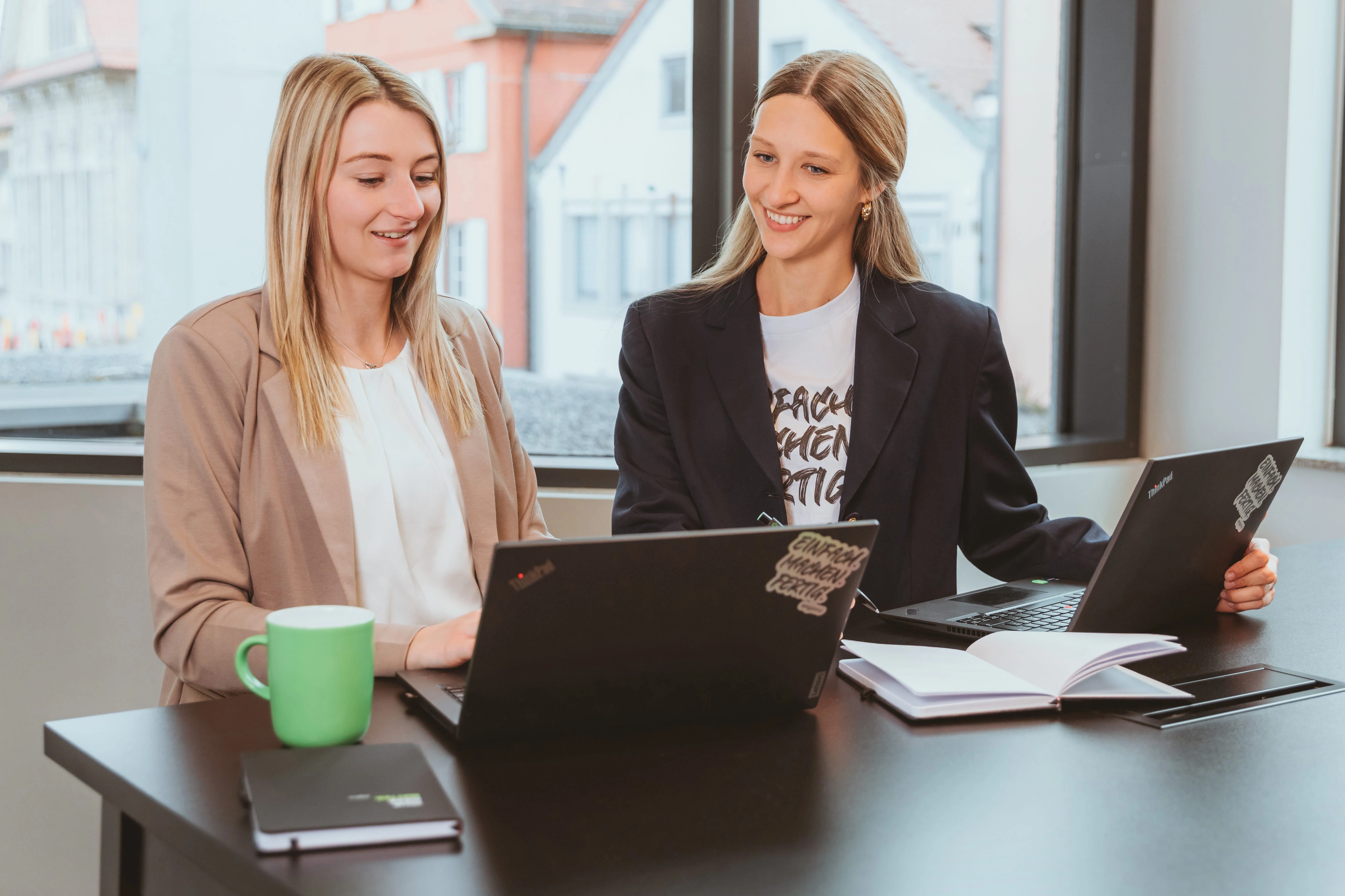 Da Bild zeigt zwei lächelnde Personen stehend an einem Tisch