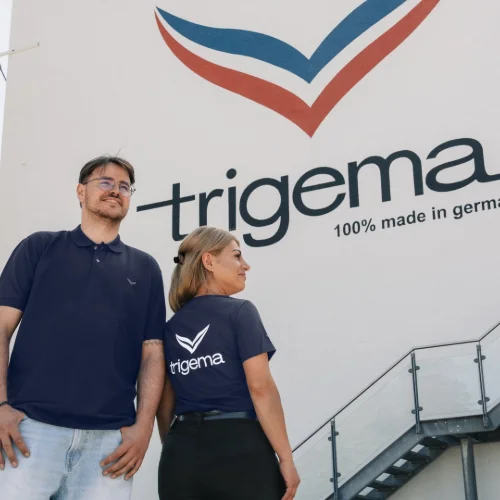 Ein Bild, das zwei trigema-Modells vor einem trigema Fabrikgeb&auml;ude zeigt