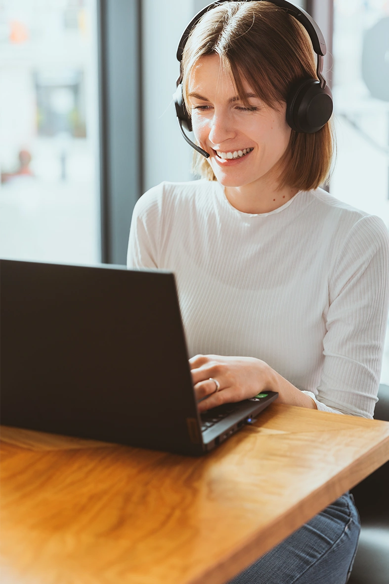 Woman wearing a headset, smiling while looking at a screen.