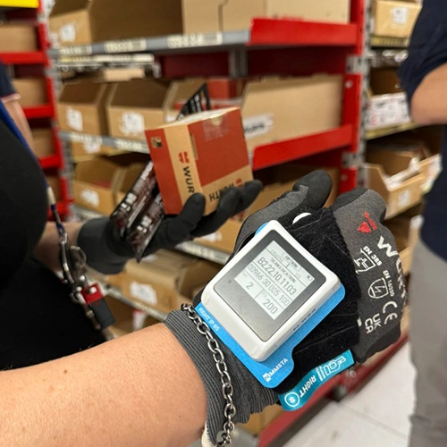 Lagermitarbeiter mit Handschuhen nutzt eine Industrial Smart Watch zur Barcode-Erfassung beim Kommissionieren vor Regalen mit Kartonware im Lager bei W&uuml;rth Italien.