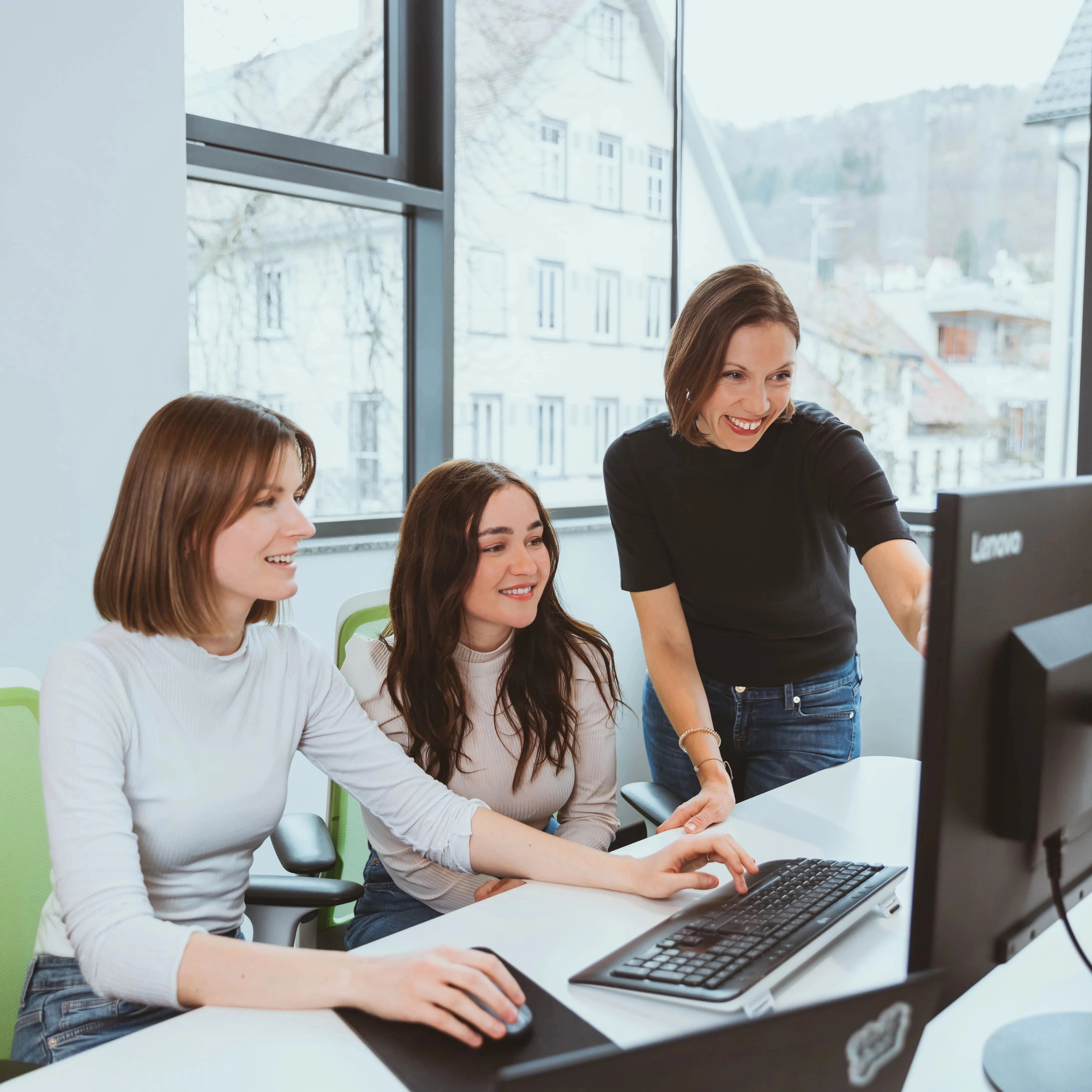 Drei Mitarbeiterinnen arbeiten gemeinsam an einem Computer in einem Büro.