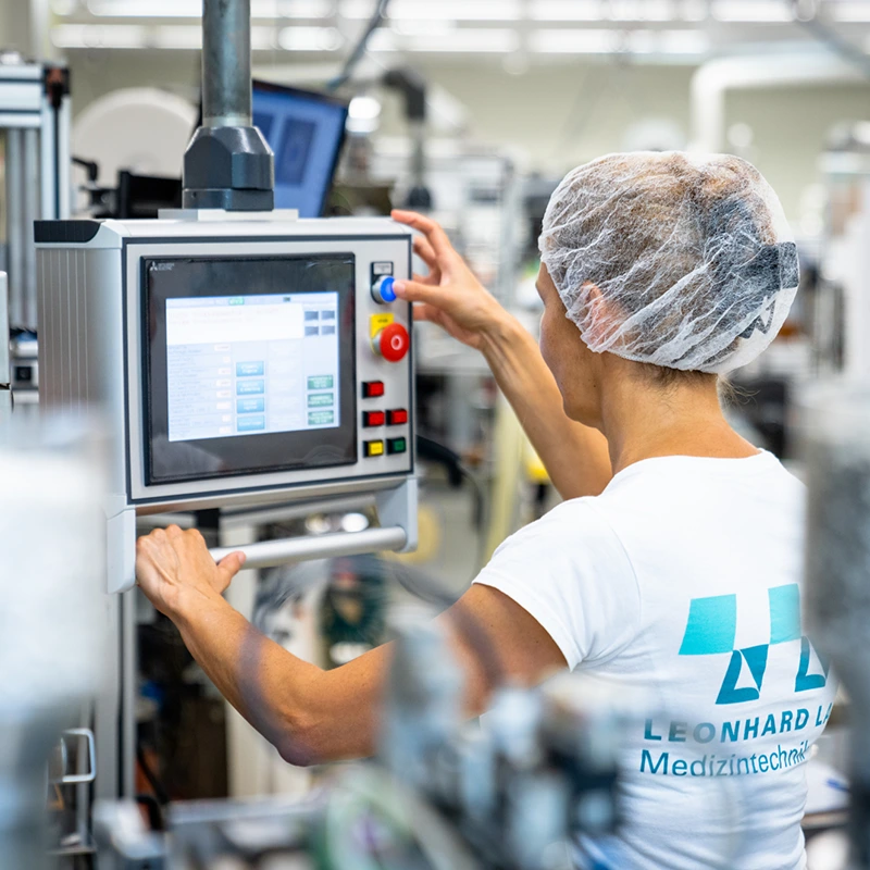 Produktionsmitarbeiterin mit Haarnetz bedient eine industrielle Maschine über ein Touchscreen-Panel in einer modernen Fertigungsanlage.