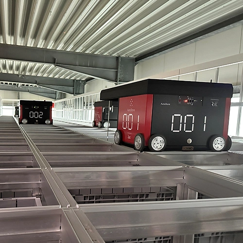 Two red AutoStore™ robots driving on a warehouse grid structure beneath an industrial ceiling – automated intralogistics solution at RIMPLER.