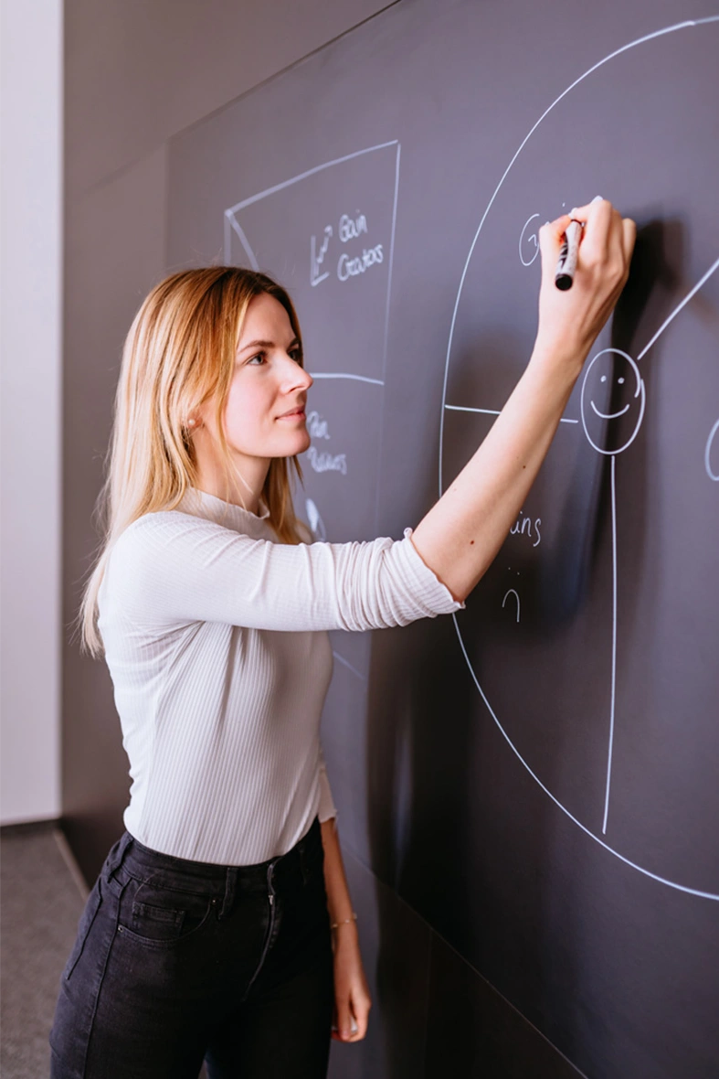 Das Bild zeigt eine Frau von der Seite, die mit einem Stift eine Zeichnung auf einer Wand skizziert