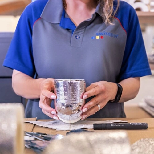 A swisspor employee holds a piece of insulation wrapped in aluminum foil while preparing it further at a workstation in the production area.